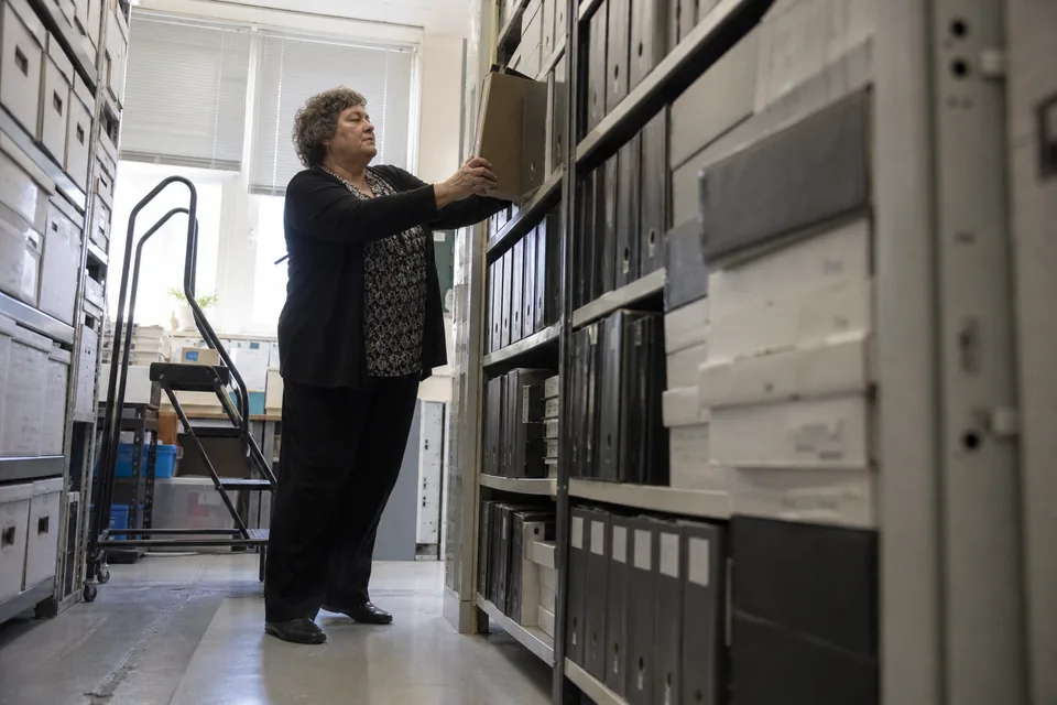 Archive room with shelves of bound state filings and a clerk pulling a binder